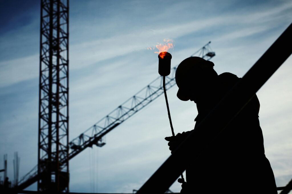 Kıdem Tazminatı, Şartları ve Hesaplanması Silhouette of a construction worker using a blowtorch at a building site against a crane-filled skyline.